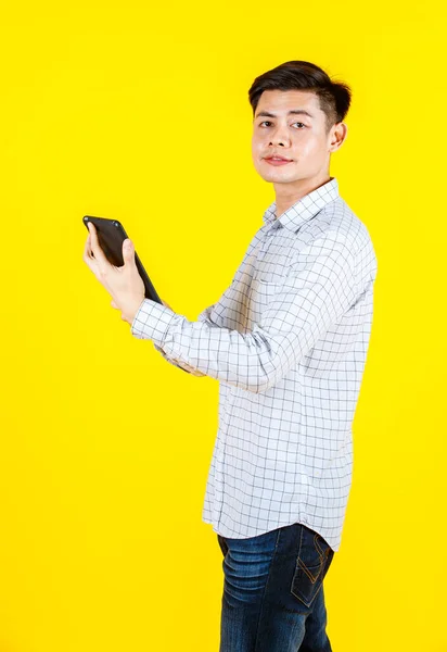 黄色の背景にノートパソコンを保持笑顔立ってカジュアルな服装で千年のアジアの若い男性実業家の肖像画スタジオショット — ストック写真