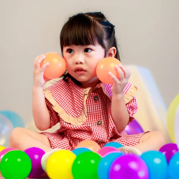 Küçük şirin anaokulu çocuğu, kırmızı uzun elbiseli, gülümseyen, gri arka planda renkli helyum hava balonlarıyla oynayan kız çocuğunun portresi..