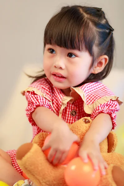 小可爱的幼稚园小女孩身穿红色婚纱 坐在地板上笑着抱着泰迪熊娃娃 在灰色背景下玩彩色塑料球 特写特写特写拍摄室 — 图库照片