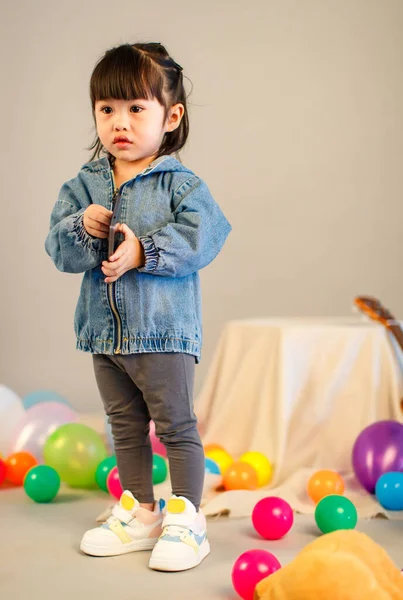Küçük şirin, masum anaokulu anaokulu kızının resmi. Sıradan bir sokakta kot ceket giyiyor. Gri arka planda elinde akıllı telefonuyla kameraya bakıyor..