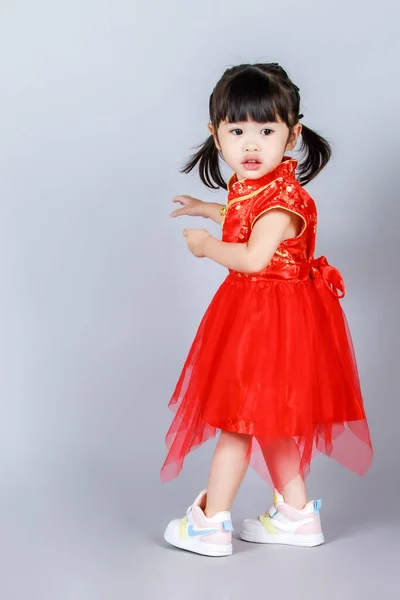 工作室全身而退 身穿传统东方红旗袍的幼女幼稚园小女儿身着灰色背景婚纱 期待着中国新年的到来 — 图库照片