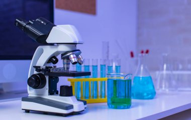 Büyüteç yakınlaştırıcı mercek mikroskop kamerasının yakın çekim görüntüleri hastane laboratuvarındaki çalışma masasının üzerine yerleştirilmiş cam teçhizat test tüpü rafı Erlenmeyer cep şişesi ve bilgisayar monitörü..