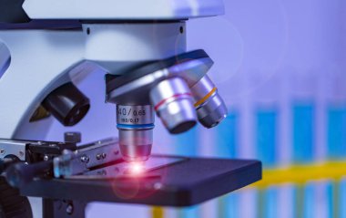 Büyüteç yakınlaştırıcı mercek mikroskop kamerasının yakın çekim görüntüleri hastane laboratuvarındaki çalışma masasının üzerine yerleştirilmiş cam teçhizat test tüpü rafı Erlenmeyer cep şişesi ve bilgisayar monitörü..