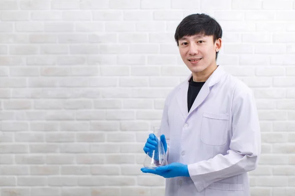 화실에서는 가운을 아시아의 직업적 과학자가 마이어 플라스크 제품을 모습으로 웃으며 — 스톡 사진