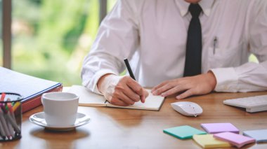 İdari müdür jot, pazarlama analizi için strateji planlaması yaparken bilgisayar faresi, klavye, yapışkan not ve bir fincan kahvenin yanında kağıt rapor üzerine işletme finansmanının kaydını tutuyor..