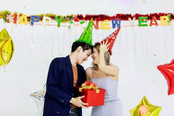 数百万人の若い恋人カップルアジアの夫でカジュアルスーツと美しい妻笑顔開催赤ラッププレゼントギフトボックス祝う幸せな新年パーティーでフル装飾された部屋で星の風船 — ストック写真