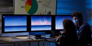 Beyaz erkek hisse senedi yatırımcısı, Afrika kökenli Amerikalı kadın iş kadınıyla konuşuyor. Tekerlekli sandalyede oturmuş, maske takıyor ve grafik analiz ekranları ve monitörlerle ticaret yapıyor..