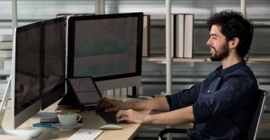Kafkasyalı mutlu erkek sakallı tüccar yatırımcı gülümseyen serbest çalışan ev ofisinde çalışan bilgisayarın verilerini yazan müşteri ve müşteri alım-satım borsası satan.