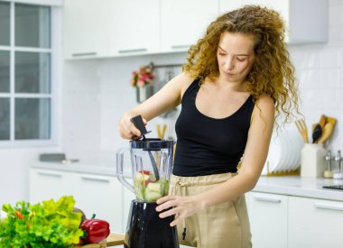 Sağlıklı kıvırcık saç stili seksi Kafkas hamile anne gündelik kıyafetlerle yemek karıştırıcı karıştırıcı karışımı ve evde mutfakta sebze diyeti kullanarak hazırlanıyor..