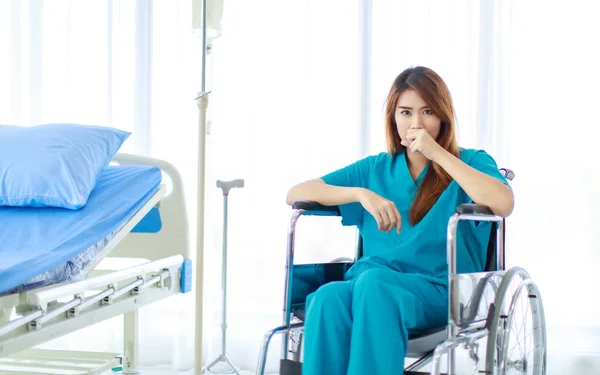 青い緑の病院の制服を着た若いアジアの女性患者の肖像画一人で座っているベッドと臨床生理食塩水スタンドで車椅子のカメラを見て頭痛の種 — ストック写真