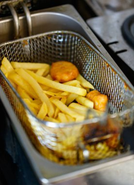 Lezzetli, lezzetli, taze, lezzetli fast food aperatifleri altın yağlı patates kızartmaları ve paslanmaz çelik pişirme sepetinde yağlı tavuk nuggetları otomatik yağ kızartma makinesinde..