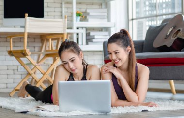 İki bin yıllık Asyalı genç, sağlıklı, sağlıklı, güçlü, seksi, spor modelleri gündelik ürünler giyip halı döşemesine uzanmış, dizüstü bilgisayardan yoga pilates dersi öğreniyorlar..