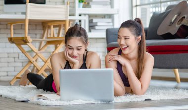 İki bin yıllık Asyalı genç, sağlıklı, sağlıklı, güçlü, seksi, spor modelleri gündelik ürünler giyip halı döşemesine uzanmış, dizüstü bilgisayardan yoga pilates dersi öğreniyorlar..