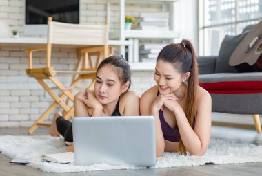 İki bin yıllık Asyalı genç, sağlıklı, sağlıklı, güçlü, seksi, spor modelleri gündelik ürünler giyip halı döşemesine uzanmış, dizüstü bilgisayardan yoga pilates dersi öğreniyorlar..