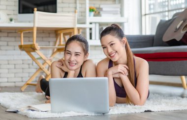 İki bin yıllık Asyalı genç, sağlıklı, sağlıklı, güçlü, seksi, spor modelleri gündelik ürünler giyip halı döşemesine uzanmış, dizüstü bilgisayardan yoga pilates dersi öğreniyorlar..