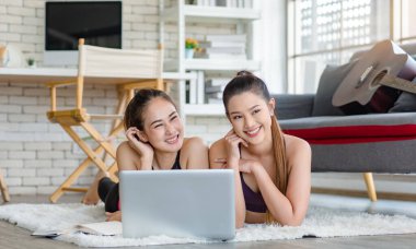 İki bin yıllık Asyalı genç, sağlıklı, sağlıklı, güçlü, seksi, spor modelleri gündelik ürünler giyip halı döşemesine uzanmış, dizüstü bilgisayardan yoga pilates dersi öğreniyorlar..