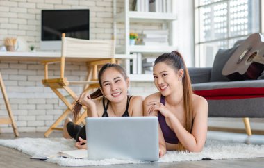 İki bin yıllık Asyalı genç, sağlıklı, sağlıklı, güçlü, seksi, spor modelleri gündelik ürünler giyip halı döşemesine uzanmış, dizüstü bilgisayardan yoga pilates dersi öğreniyorlar..