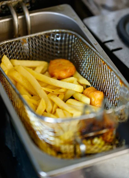 Lezzetli, lezzetli, taze, lezzetli fast food aperatifleri altın yağlı patates kızartmaları ve paslanmaz çelik pişirme sepetinde yağlı tavuk nuggetları otomatik yağ kızartma makinesinde..