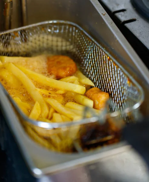 Lezzetli, lezzetli, taze, lezzetli fast food aperatifleri altın yağlı patates kızartmaları ve paslanmaz çelik pişirme sepetinde yağlı tavuk nuggetları otomatik yağ kızartma makinesinde..