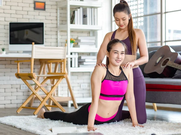 Asyalı, genç, sağlıklı, güçlü, seksi, spor hocası, spor kıyafetleri içinde. Oturma odasındaki özel sınıftaki halı zemininde gerinen öğrencilere yoga öğretmeye yardım ediyor..