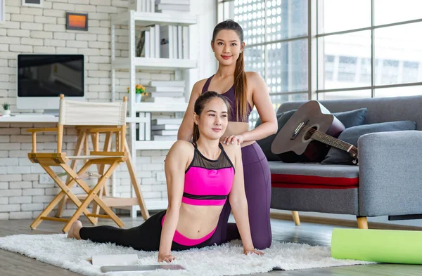 Asyalı, genç, sağlıklı, güçlü, seksi, spor hocası, spor kıyafetleri içinde. Oturma odasındaki özel sınıftaki halı zemininde gerinen öğrencilere yoga öğretmeye yardım ediyor..