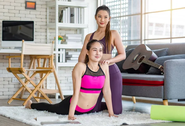 Asyalı, genç, sağlıklı, güçlü, seksi, spor hocası, spor kıyafetleri içinde. Oturma odasındaki özel sınıftaki halı zemininde gerinen öğrencilere yoga öğretmeye yardım ediyor..