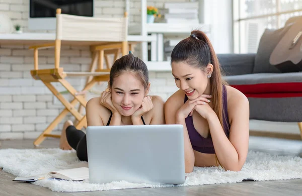 İki bin yıllık Asyalı genç, sağlıklı, sağlıklı, güçlü, seksi, spor modelleri gündelik ürünler giyip halı döşemesine uzanmış, dizüstü bilgisayardan yoga pilates dersi öğreniyorlar..