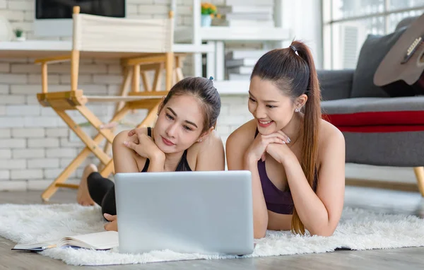 İki bin yıllık Asyalı genç, sağlıklı, sağlıklı, güçlü, seksi, spor modelleri gündelik ürünler giyip halı döşemesine uzanmış, dizüstü bilgisayardan yoga pilates dersi öğreniyorlar..