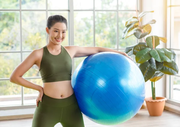 Milenyum Asyalı genç, sağlıklı, sağlıklı, güçlü, seksi kadın spor model, günlük kıyafetleri içinde, güler yüzlü, yoga minderinde egzersiz topuna el ele tutuşmuş, stüdyoda çalışmaya hazır..