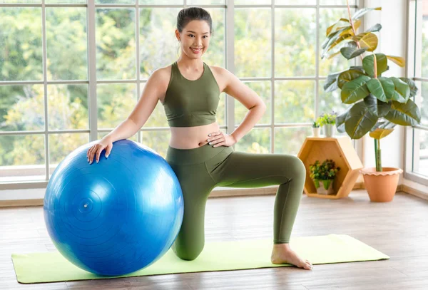 Milenyum Asyalı genç, sağlıklı, sağlıklı, güçlü, seksi kadın spor model, günlük kıyafetleri içinde, güler yüzlü, yoga minderinde egzersiz topuna el ele tutuşmuş, stüdyoda çalışmaya hazır..