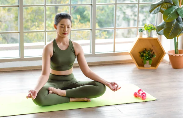 Asyalı, genç, güzel, seksi, zayıf, güçlü spor model. Ekinler içinde, üst üste spor giyimli, bacak bacak üstüne atmış, Lotus pozisyonunda meditasyon yapan, hafif ışık efektiyle sınıfın spor salonundaki yoga minderi..