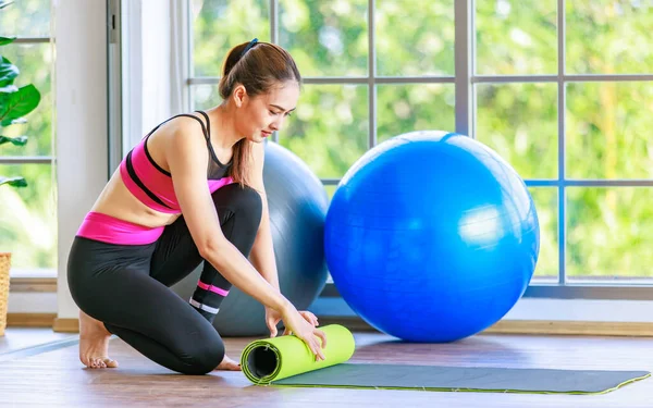 Asyalı, genç, sağlıklı, güzel, sportif model, spor kıyafetleri içinde, cam camlı spor salonunda, yuvarlanan yoga minderinde gülümseyen, jimnastik salonu aerobik sınıfında, pilates egzersiz toplarıyla birlikte..