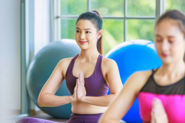 İki Milenyum Asyalı genç, sağlıklı, zayıf, güçlü, seksi spor modelleri, günlük kıyafetleri içinde, spor kıyafetleri içinde, gülümseyen, göğüs kafesinde oturmuş, pilates yoga salonu stüdyosunda meditasyon yaparken..
