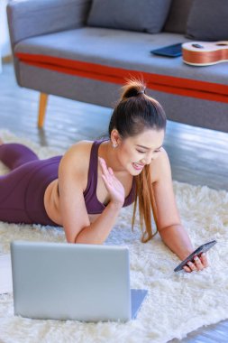 Milenyum Asyalı genç, sağlıklı, zayıf, güçlü, seksi, spor modelleri gündelik ürünler giyip, oturma odasında halı döşemesine uzanmış, akıllı telefon görüşmeleri yapıp arkadaşınla selamlaşıyorsun..