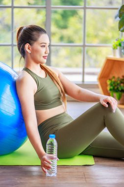 Millennial Asyalı genç, sağlıklı, sağlıklı kadın spor modelinin spor kıyafetleri içinde spor topunun üzerinde oturmuş spor yaparken gülümseyerek sınıfın spor salonundaki çene atölyesinde el ele poz verirken yakın çekim..