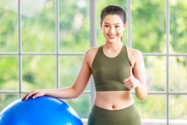 Milenyum Asyalı genç, sağlıklı, sağlıklı, güçlü, seksi kadın spor model, günlük kıyafetleri içinde, güler yüzlü, yoga minderinde egzersiz topuna el ele tutuşmuş, stüdyoda çalışmaya hazır..