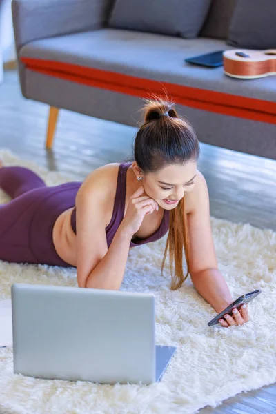 Milenyum Asyalı genç, sağlıklı, zayıf, güçlü, seksi, spor modelleri gündelik ürünler giyip, oturma odasında halı döşemesine uzanmış, akıllı telefon görüşmeleri yapıp arkadaşınla selamlaşıyorsun..