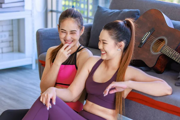 İki Milenyum Asyalı genç, güzel, sağlıklı, sağlıklı, güçlü, seksi, spor modelleri gündelik ürünler giyip spor kıyafetleri giyip salonda birlikte oturup, Safa 'da akustik gitarla sohbet ediyorlar..