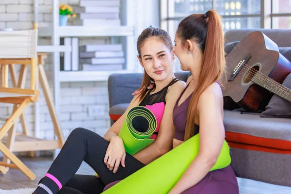 İki Milenyum Asyalı genç, sağlıklı, sağlıklı, güçlü, seksi kadın spor modelleri gündelik ürünler, spor kıyafetleri içinde yere oturmuş gülümsüyor yoga minderlerini bir arada tutarak oturma odasında kanepede gitarla birlikte oturuyorlar..
