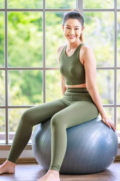 Milenyum Asya 'lı genç, sağlıklı, sağlıklı, güçlü, seksi, spor modelleri, günlük ürünler, spor kıyafetleri içinde gülümseyerek yoga minderinde Malasana pozu veriyorlar. Pilates sınıfı stüdyosunda.