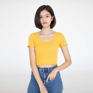 Asyalı, arkadaş canlısı, kısa saçlı bir genç kızın, sıradan bir bluz ve kot pantolonla beyaz arka planda el ele tutuşup gülümserken çekilmiş bir portresi..