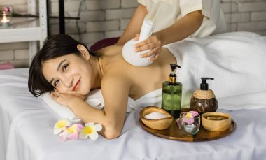 Asyalı genç, güzel bir spa müşterisi sırt ve omuz masajı yaparken masaj yatağında kameraya gülümseyip tanınmaz hale gelen profesyonel kadın masajcı..