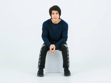 Uzun kollu gömlek, kumaş pantolon ve beyaz arka planda poz veren spor ayakkabı giyen Asyalı genç, yakışıklı, kendine güvenen, sağlıklı erkek modelin tam vücut çekimi..