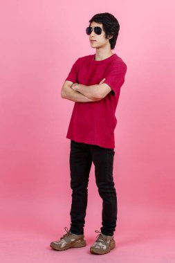Asyalı genç şehirli erkek modelin günlük sokak tarzı tişört ve siyah kot ve havacı güneş gözlüklü pembe arka planda kameraya poz verirken çekilmiş bir portre fotoğrafı..
