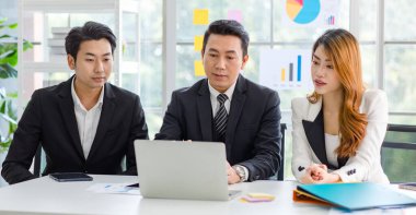 Bir grup neşeli Asya milenyum profesyonel başarılı erkek işadamı ve resmi takım elbiseli kadın işkadını oturmuş gülümseyip yumruklarını sallayarak müşteri anlaşmasını kutluyorlar..