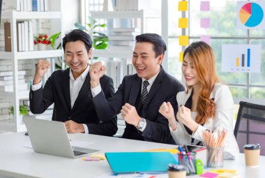 Group of cheerful Asian millennial professional successful male businessman and female businesswoman in formal suit sitting smiling holding fists up together celebrating customer agreement deal done.