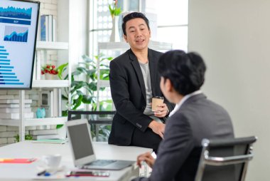 Asyalı, profesyonel, başarılı, sıradan takım elbiseli bir erkek işadamı kahve molası verir. Ofisteki tanınmayan iş arkadaşıyla konuşur..