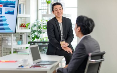 Asyalı, profesyonel, başarılı, sıradan takım elbiseli bir erkek işadamı kahve molası verir. Ofisteki tanınmayan iş arkadaşıyla konuşur..