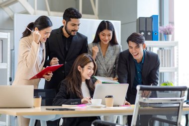 Multicultural multinational millennial Asian female businesswomen Indian male businessman boss in formal suit helping working brainstorming together with laptop computer in conference meeting room.