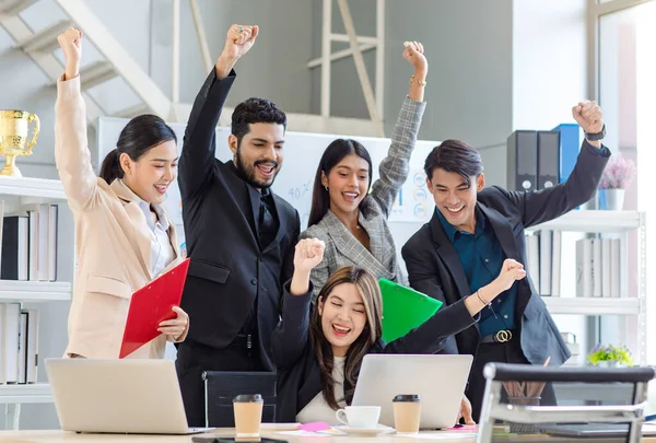 Group of multicultural multinational successful professional cheerful male female businessman businesswoman in formal suit sitting standing smiling holding fists up celebrate job achievement together.